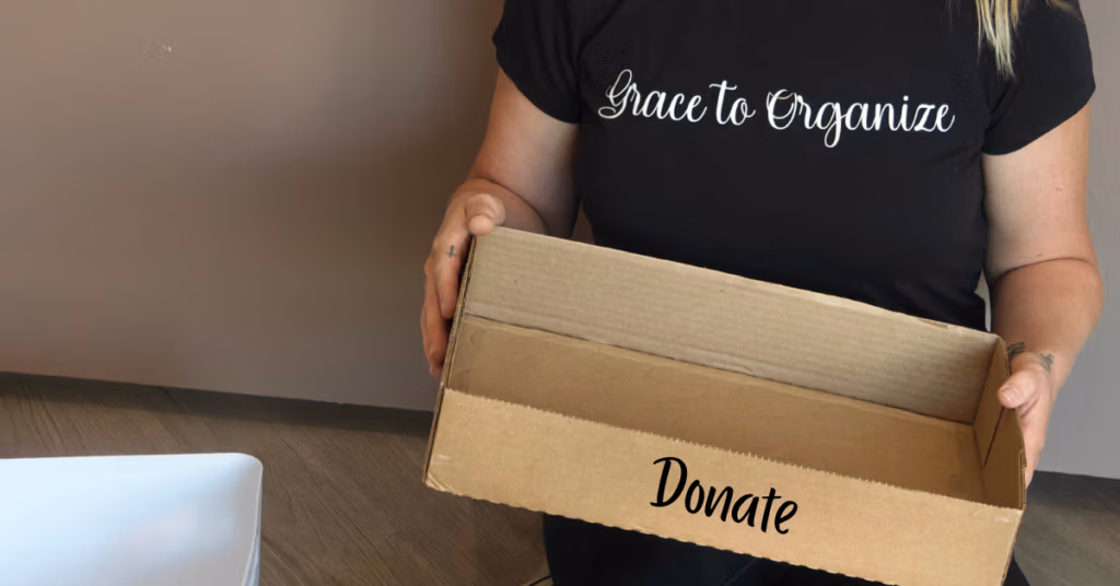 Person holding a box ready for donated items during a decluttering session.
